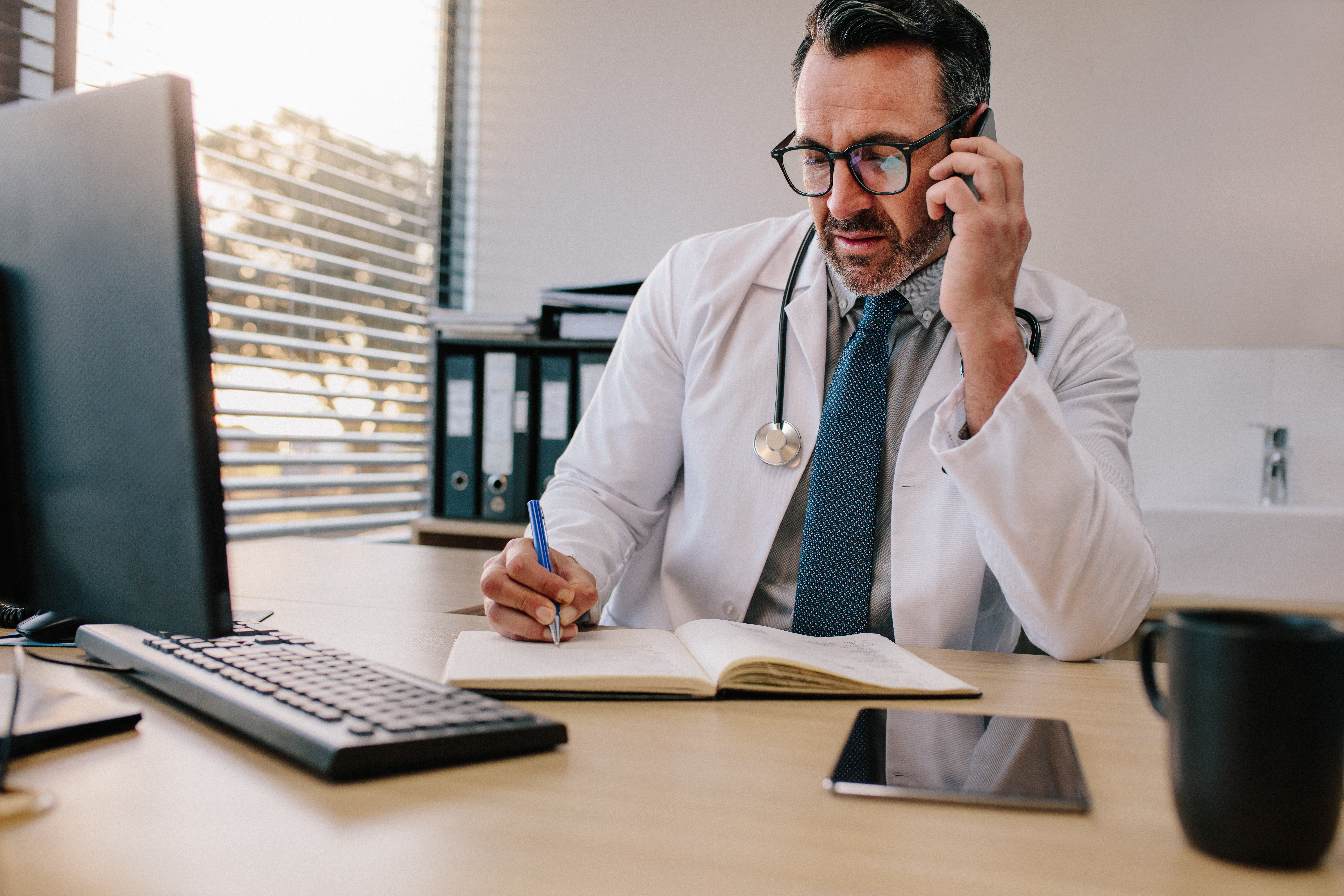 A physician mentor on the phone while reviewing notes at a desk.