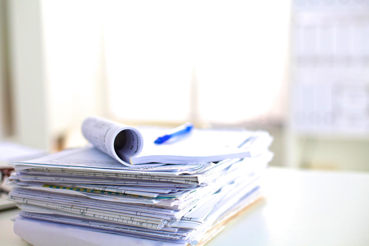 A stack of research papers on a desk in bright natural light.